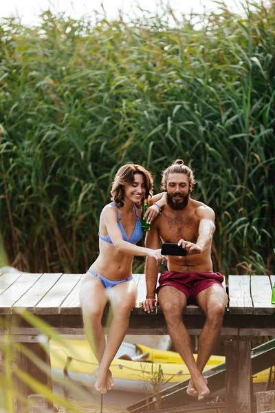 Genç adam ve cep telefonu kamera ile selfie alarak ve yaz Nehri üzerinde zevk kadın.