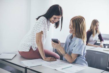 İki gülümseyen kız lise sınıf oturma ve cep telefonu arıyorum.