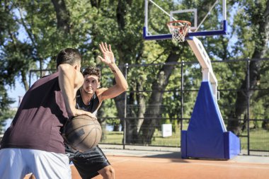 Açık sahada basketbol oynarken iki genç adam.