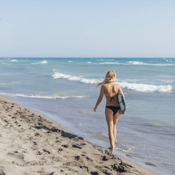 砂浜の上を歩く金髪の女性サーファーの背面図 — ストック写真