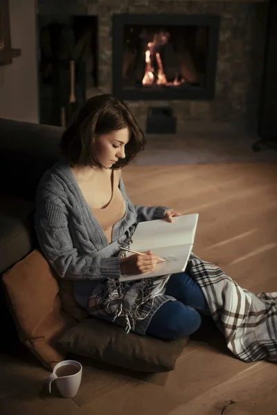 Piękna Kobieta Siedząc Przy Kominku Przytulnym Sweter Pisanie Notesie — Zdjęcie stockowe