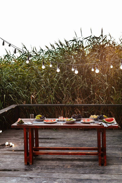 Food served on wooden table for outdoor dinner party.
