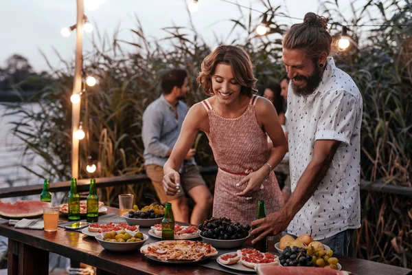 きれいな女性とハンサムな男が夏の屋外パーティーで食品テーブルのそばに立って — ストック写真