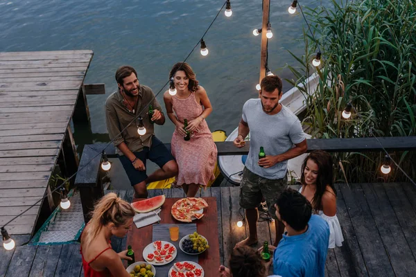 Group of young people having outdoor dinner party by the river.