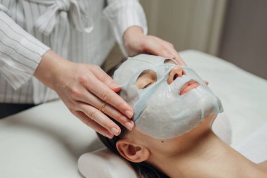 Beyaz güzellik uzmanı kadın masaj yatakta yatıyordu bir güzel genç beyaz kadının yüzüne bir yüz maskesi koyarak.