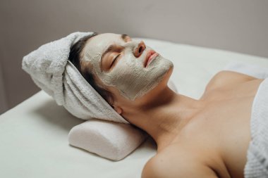 Güzel genç beyaz bir kadın Masaj masanın üzerinde yatan yüzünde doğal yüz maskesi.