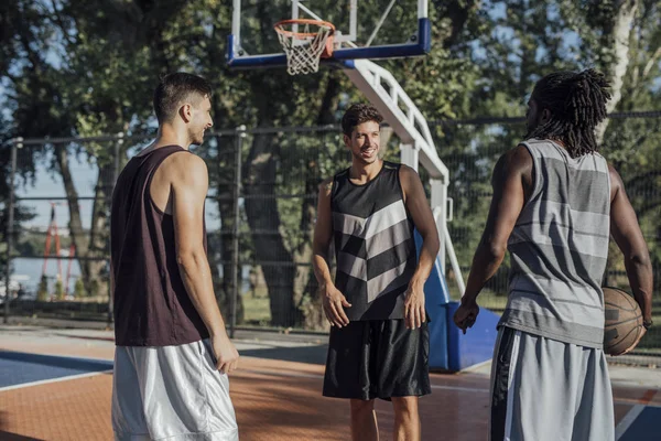 Three handsome friends and basketball players laughing and having fun on an outdoor basketball court.
