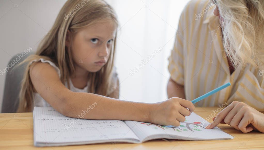Cute blonde Caucasian girl studying at home with her mother helping.