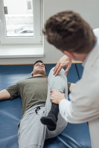 Młody Człowiek Rozciąganie Nogę Jego Lekarz Pomaga — Zdjęcie stockowe
