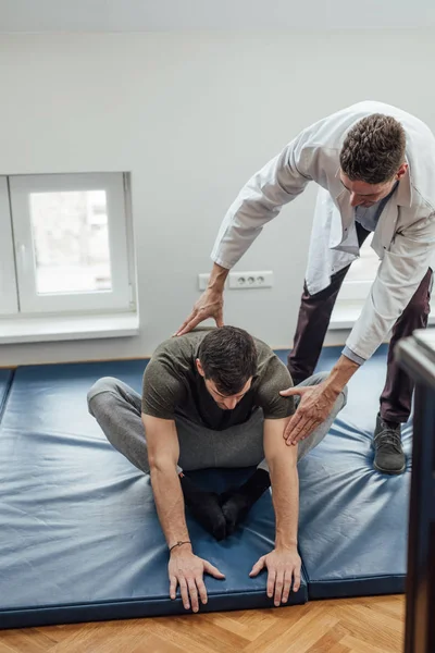 Ung Man Stretching Hans Rygg Med Hans Läkare Som Hjälper — Stockfoto