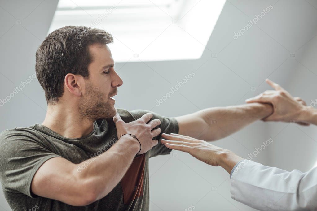 Young man stretching his arm with his physician helping.