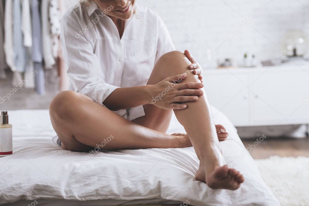 Pretty smiling Caucasian woman applying a lotion to her legs during her morning routine.