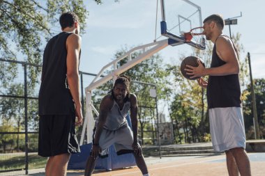 Üç yakışıklı adam açık havada basketbol oynarken.