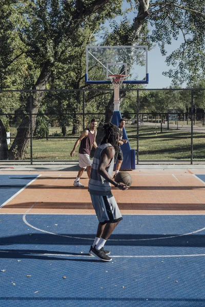 Three handsome men playing basketball outdoors.