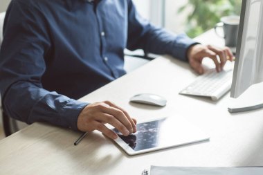 Genç işadamı modern ofis alanı, bir masaüstü bilgisayarda çalışırken tablet kullanma.