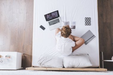 Kadın fotoğrafı yukarıda bir kitap okuma ve onun yatağında okurken onu laptop yazma.