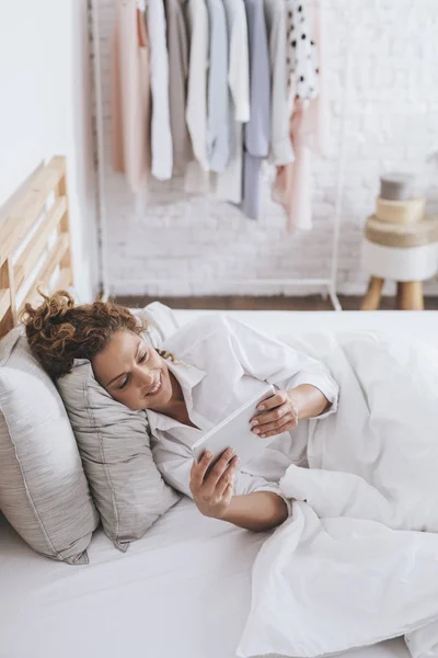 Vrij Lachende Kaukasische Vrouw Liggend Haar Bed Lezen Een Tablet — Stockfoto