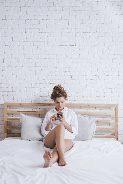 美丽的白种女人坐在她的特大床和打字的手机 — 图库照片