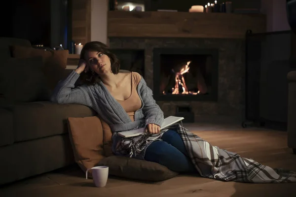 漂亮的白种女人坐在舒适的毛衣壁炉和手持笔记本 — 图库照片