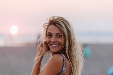 Sahilde duran ve kameraya bakıyor güzel sarışın gülümseyen kadın.