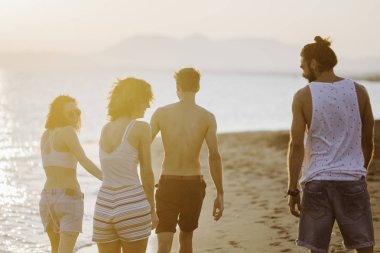 Kumlu sahilde yürüyüş ve mutlu görünüyordu kadın ve genç erkek grup.