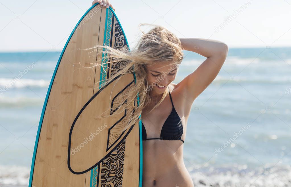 Portrait of a pretty blonde woman surfer standing on beach.