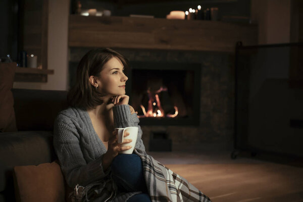 Pretty caucasian woman sitting at cozy sweater by the fireplace and holding a notebook.