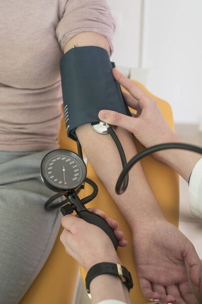 Hands of unrecognisable woman doctor measuring patient's blood pressure at hospital.