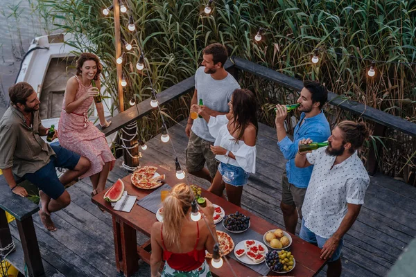 Group of young people having outdoor dinner party by the river.