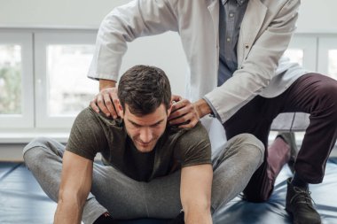 Genç adam sırtını yardım doktoru ile germe.