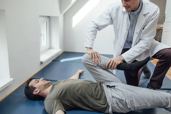 Giovane Uomo Allungando Gamba Con Suo Medico Aiutando — Foto Stock