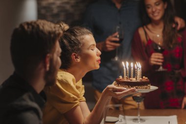 Güzel genç bayan doğum günü pastasında mum üflüyor..