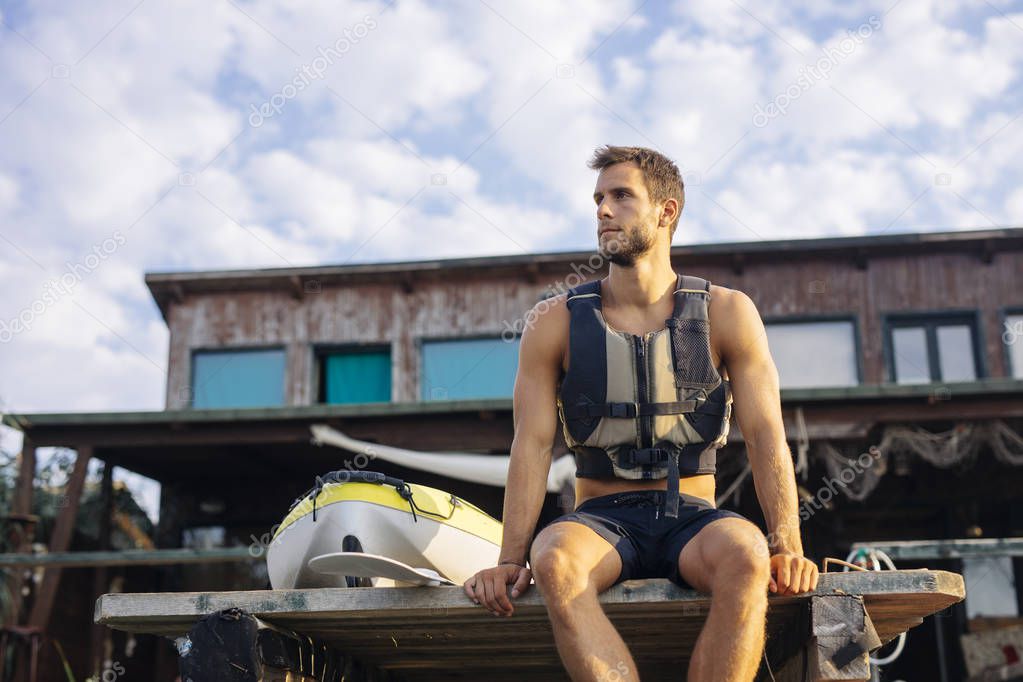Man wearing a life vest while sitting on a wooden pier.
