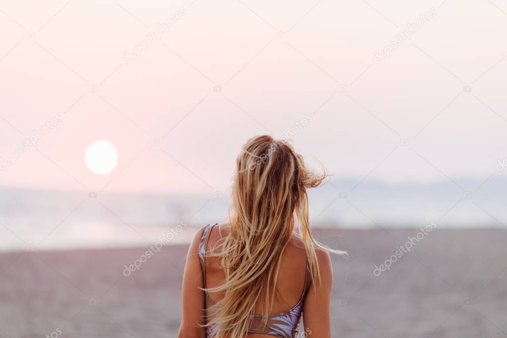 Back view of a woman standing on sandy beach.