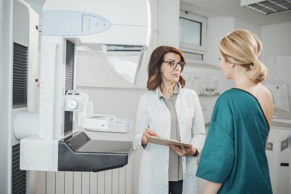 Woman oncologist talking with her patient on mammography examination.