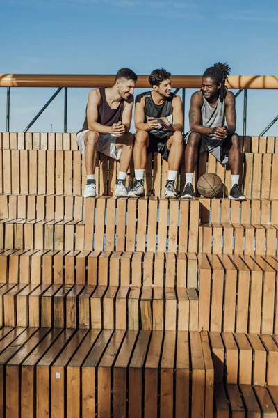 Grupo Multiétnico Jugadores Baloncesto Sentados Junto Cancha Utilizando Teléfono Celular —  Fotos de Stock