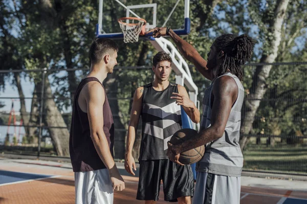 Group of young sportsmen playing basketball on outdoor court.