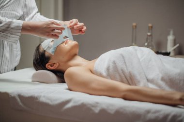 Beyaz güzellik uzmanı kadın masaj yatakta yatıyordu bir güzel genç beyaz kadının yüzüne bir yüz maskesi koyarak.