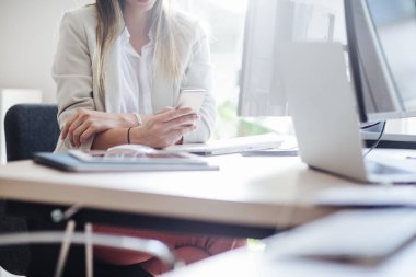 Masaüstü bilgisayar önünde bir cep telefonu modern ofis alanı kullanarak unrecognisable işkadını.