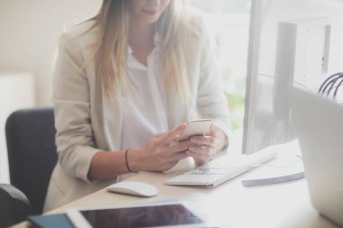 Masaüstü bilgisayar önünde bir cep telefonu modern ofis alanı kullanarak unrecognisable işkadını.