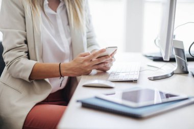 Masaüstü bilgisayar önünde bir cep telefonu modern ofis alanı kullanarak unrecognisable işkadını.