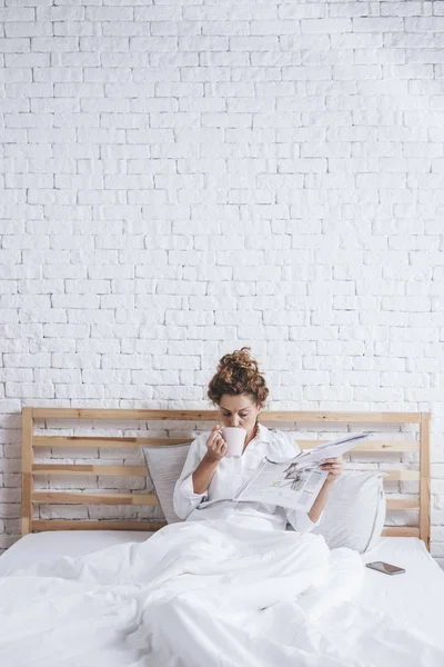 Αρκετά Καυκάσιος Γυναίκα Διαβάζοντας Εφημερίδες Και Πίνει Καφέ Στο Κρεβάτι — Φωτογραφία Αρχείου