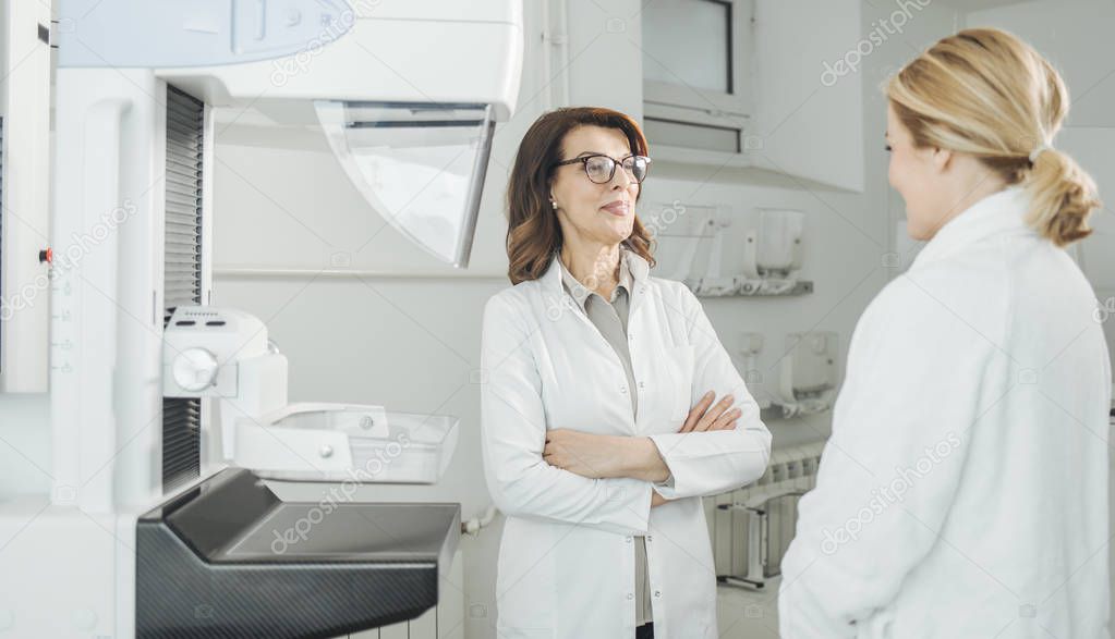 Pretty Caucasian woman doctor talking with her patient on mammography examination.