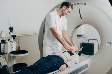 Ct tarayıcı yatakta yatıyordu ve kafasını tutarak onun hasta konuşurken genç tıbbi teknisyen.