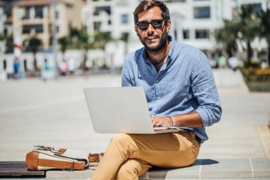 Bankta oturan ve onun dizüstü bilgisayarda çalışan yakışıklı beyaz adam serbest meslek.