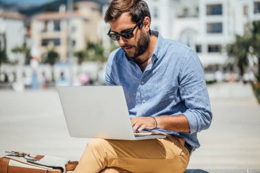 Bankta oturan ve onun dizüstü bilgisayarda çalışan yakışıklı beyaz adam serbest meslek.