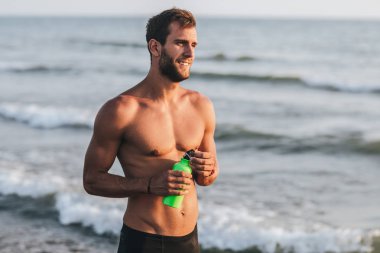 Yakışıklı sporcu kumsalda ayakta portresi.