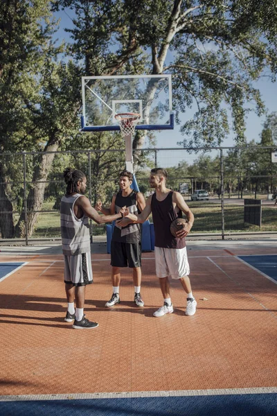 3名年轻男子站在室外篮球场上使用手机 — 图库照片