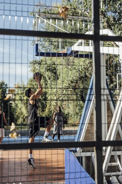 Three young men playing basketball on an outdoor basketball court.