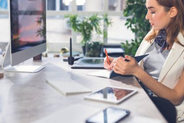 Modern ofiste oturan ve onun not defterinde yazılı genç iş kadını.
